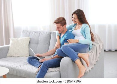 Happy couple with credit card sitting on sofa and making online shopping