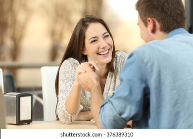 Happy couple dating and flirting and holding hands together in a coffee shop with a sunset light outdoor in the background