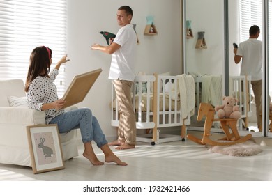 Happy Couple Decorating Baby Room With Pictures Together. Interior Design