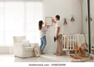 Happy Couple Decorating Baby Room With Pictures Together. Interior Design