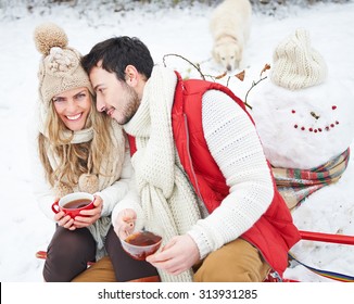 Happy Couple With Dog Drinking Tea In Winter Sitting On A Sled