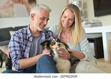 Happy Couple With Dog Relaxing At Home, Sitting On Carpet