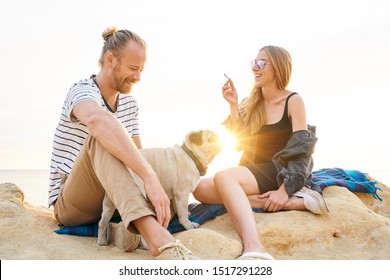 Happy Couple With A Dog Smoking Marijuana Joint By The Sea At Sunset