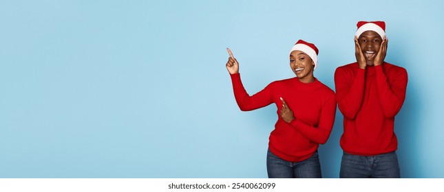 A happy couple dressed in red shirts and Santa hats shares a moment of joy as they point and celebrate the festive season, embodying the spirit of Christmas with smiles and excitement, copy space - Powered by Shutterstock