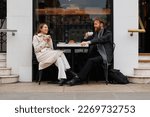 Happy couple drinking coffee and laughing talking to each other sitting at the table of outdoor cafe on city streets