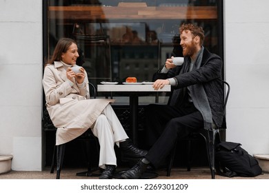 Happy couple drinking coffee and laughing talking to each other sitting at the table of outdoor cafe on city streets - Powered by Shutterstock