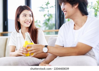 Happy Couple Drinks Orange Juice On Comfortable Couch At Home. People Leisure Activities And Lifestyle