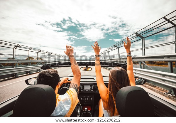 Happy couple driving a convertible car enjoying\
vacation having fun on the\
road