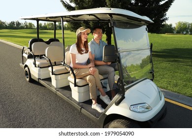 Happy Couple Driving Golf Cart On Road In Park