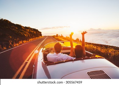 Happy Couple Fahren auf der Landstraße in den Sonnenuntergang im klassischen Vintage Sports Car