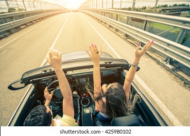 Happy Couple Driving On The Road Into The Sunset In A Sports Car