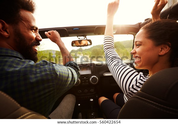Happy\
couple driving in their car with arms in the\
air