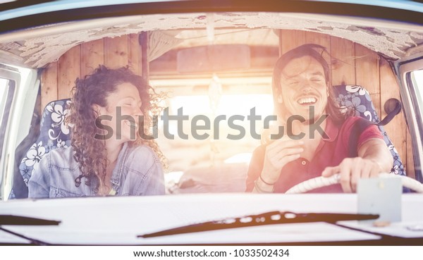 Happy couple driving vintage minivan for a summer road
trip - Trendy people having fun on holiday vacation traveling
around the world - Travel,love and hippie lifestyle concept - Focus
on faces 