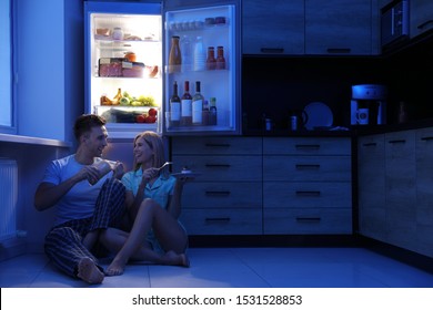 Happy Couple Eating Near Refrigerator In Kitchen At Night