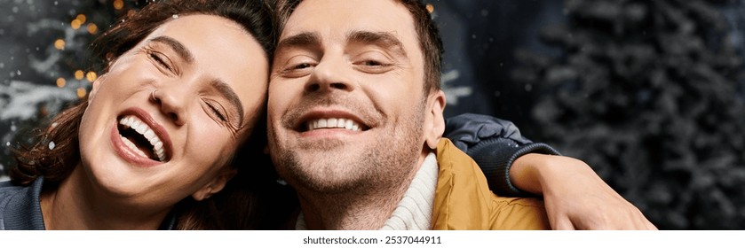 A happy couple embraces the spirit of Christmas in warm jackets while surrounded by snow-covered pine trees. - Powered by Shutterstock