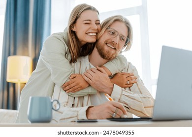 Happy couple embraces in their cozy home office, smiling and enjoying a break together. They balance work and love, surrounded by technology and warmth. Relationship concept - Powered by Shutterstock