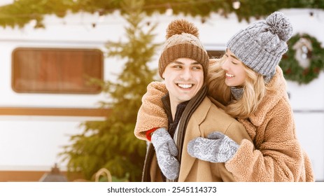 A happy couple embraces in the winter snow, surrounded by a festive atmosphere. They wear warm clothing and smile joyfully while playing outside by a camper van decorated for the season. - Powered by Shutterstock