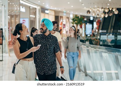 Happy Couple Embracing And Using Mobile Phone Together While Carrying Shopping Bags At The Shopping Mall - Powered by Shutterstock