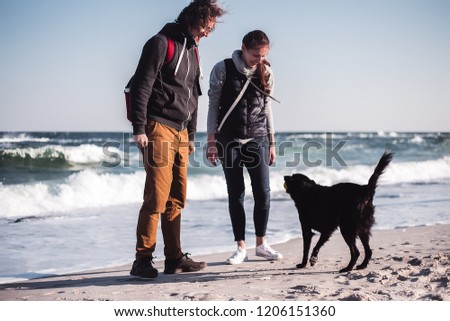 Happy couple enjoy sea with a dog, hipster guy walking at the sea, casual clothes, trendy outfit, curly hair, freedom, man standing at the beach, alone, brown pants, wild boy, emotions, love, ball