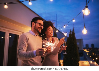 Happy Couple Enjoying Drinks And Balcony Party.