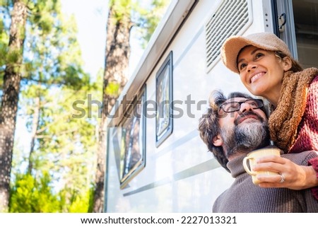 Happy couple enjoying outdoor forest destination smiling together outside their camper van vehicle. Concept of alternative travel vacation and free off grid lifestyle. People traveler with motorhome