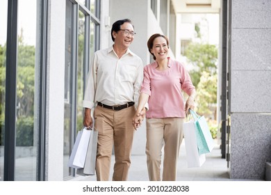 Happy couple enjoying vacation, they are holding hands when walking along the street after shopping