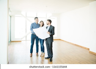 Happy couple and estate agent discussing over blueprint in new luxury apartment