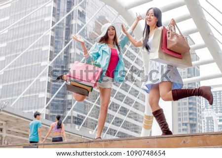 Happy couple fashionable young friend women jumping in the air with colorful shopping bags in hand after strolling and purchasing goods from stores at modern city background. business concept.