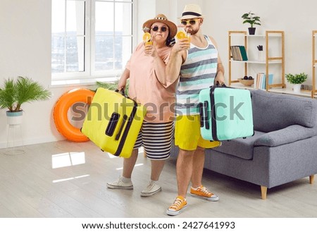 Happy couple of fat woman and smiling man in hats and sunglasses getting ready for holiday trip standing at home with suitcase, beach ball and rubber ring. Vacation and summer journey concept.