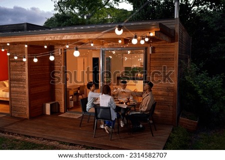 Happy couple friends enjoying dinner, toasting wine glasses at summer table on house patio with string lights