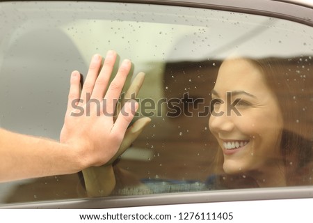 Happy couple or friends saying good bye touching hands through a car window before travel