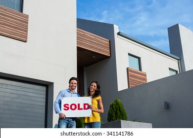 Happy Couple In Front Of New House With Sold Sign