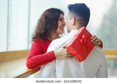 Happy couple with gift hugging. Red gift box in the hands of a couple in love. Valentine's Day, holiday and surprise concept. Lovers give each other presents. Relationship and love concept. - Shutterstock ID 1611438142