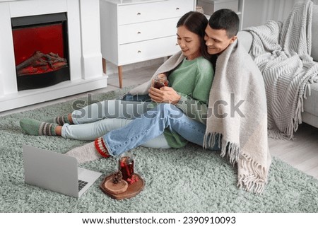 Happy couple with glasses of warm mulled wine watching movie while sitting on floor in living room