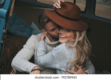 Happy couple.  Handsome young man kissing his attractive girlfriend and smiling while sitting in blue retro style mini van - Powered by Shutterstock