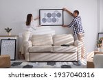 Happy couple hanging picture on white wall together. Interior design
