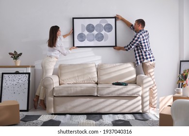 Happy couple hanging picture on white wall together. Interior design