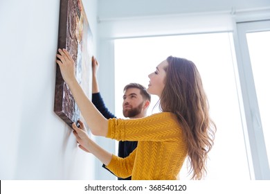 Happy couple hanging picture on the wall at home - Shutterstock ID 368540120