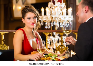 Happy Couple Have A Romantic Date In A Fine Dining Restaurant, A Large Chandelier Is In Background