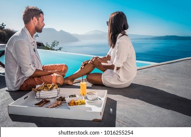 Happy couple having breakfast by the infinity pool looking out over the Caldera ocean of Santorini Greece on vacation - Powered by Shutterstock