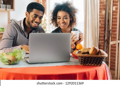 Happy Couple Having Breakfast And Watching Video On Laptop In Kitchen. Happy Sunday Morning Concept.