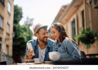 Happy couple having cup of coffee while using mobile phone in sidewalk cafe. - Powered by Shutterstock