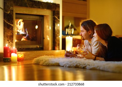 Happy couple having drinks by a fireplace in a cozy dark living room on Christmas eve