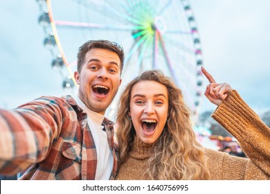 Happy couple having fun at amusement park in London - young couple in love taking a selfie and enjoying time at funfair with rollercoaster on background - Happy lifestyle and love concepts - Powered by Shutterstock