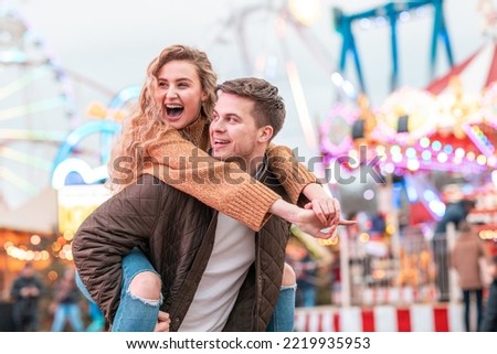 Happy couple having fun at amusement park in London - Portrait of young couple in love enjoying time at funfair with rollercoaster on background - Happy lifestyle and love concepts