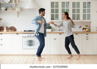 Happy Couple Having Fun Dancing Together In Modern Kitchen Enjoying Lifestyle, Active Funky Young Husband And Wife First Time Home Buyers Moving Listening Music Laughing Celebrating Freedom Party