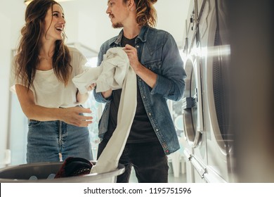 Happy couple having fun doing laundry together. Couple standing in a laundry room putting clothes in washing machine from a basket. - Powered by Shutterstock