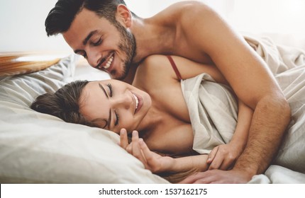 Happy couple having fun on bed under blanket - Young romantic lovers intimate moments - Intimacy and love relationship concept