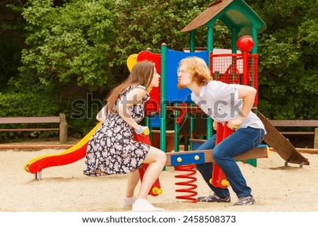 Happy couple having fun together outdoor. Happiness, great relationship. Man and woman fooling around, ride on swing at playground.
