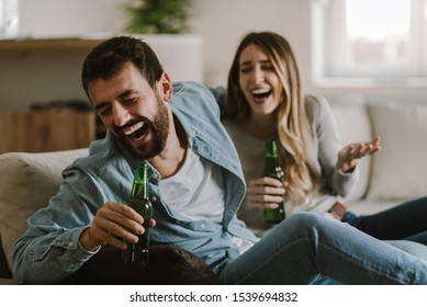 Happy Couple Having Fun While Drinking Beer At Home